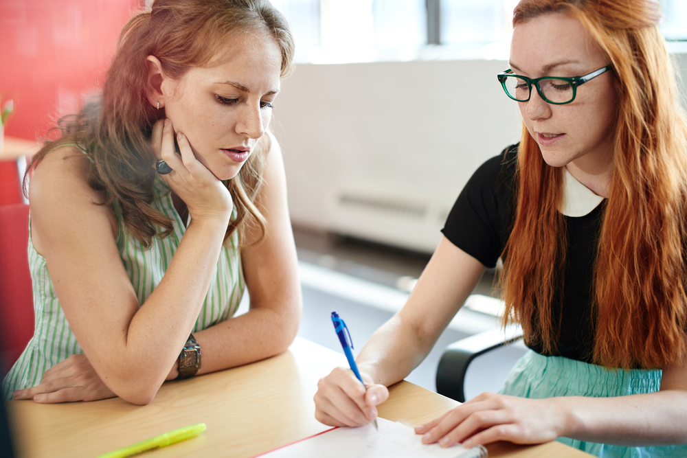 two colleagues writing something on a notepad